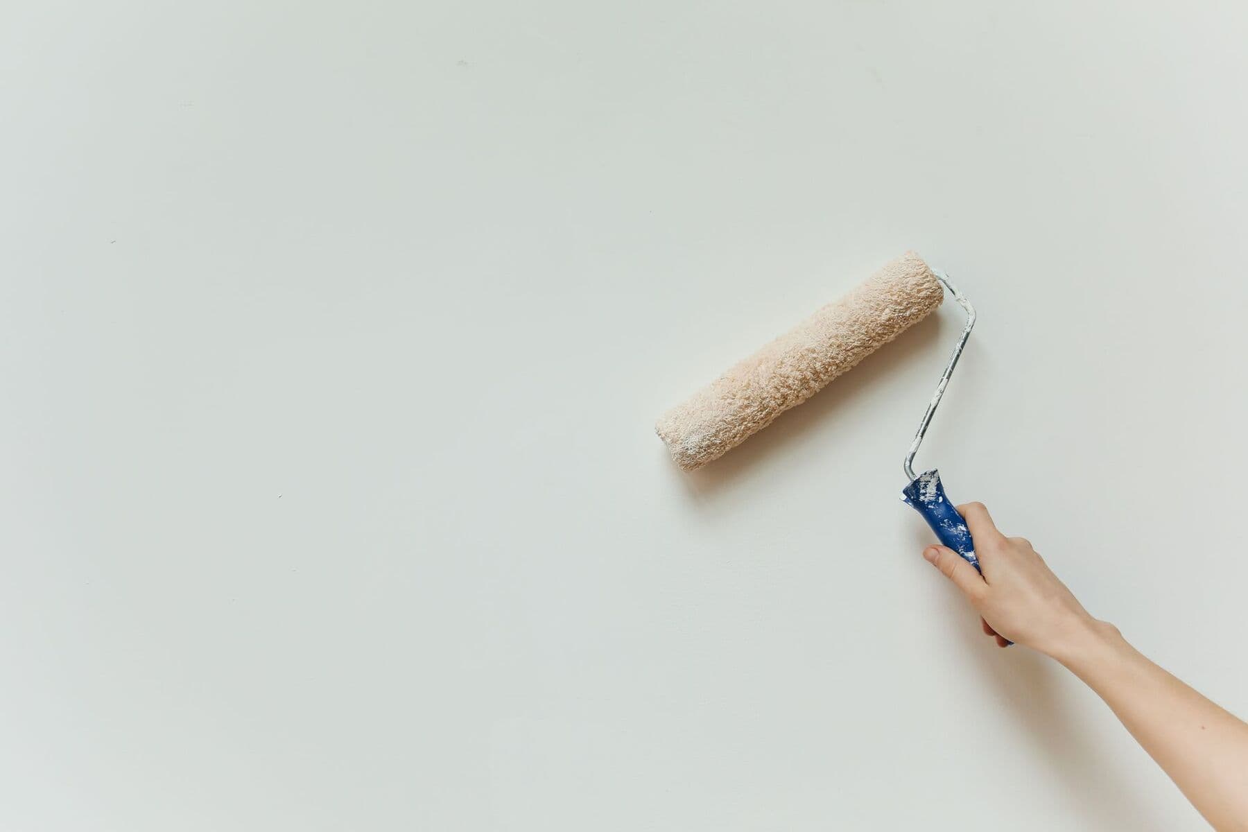 A hand pushing a paint roller across a pale wall.