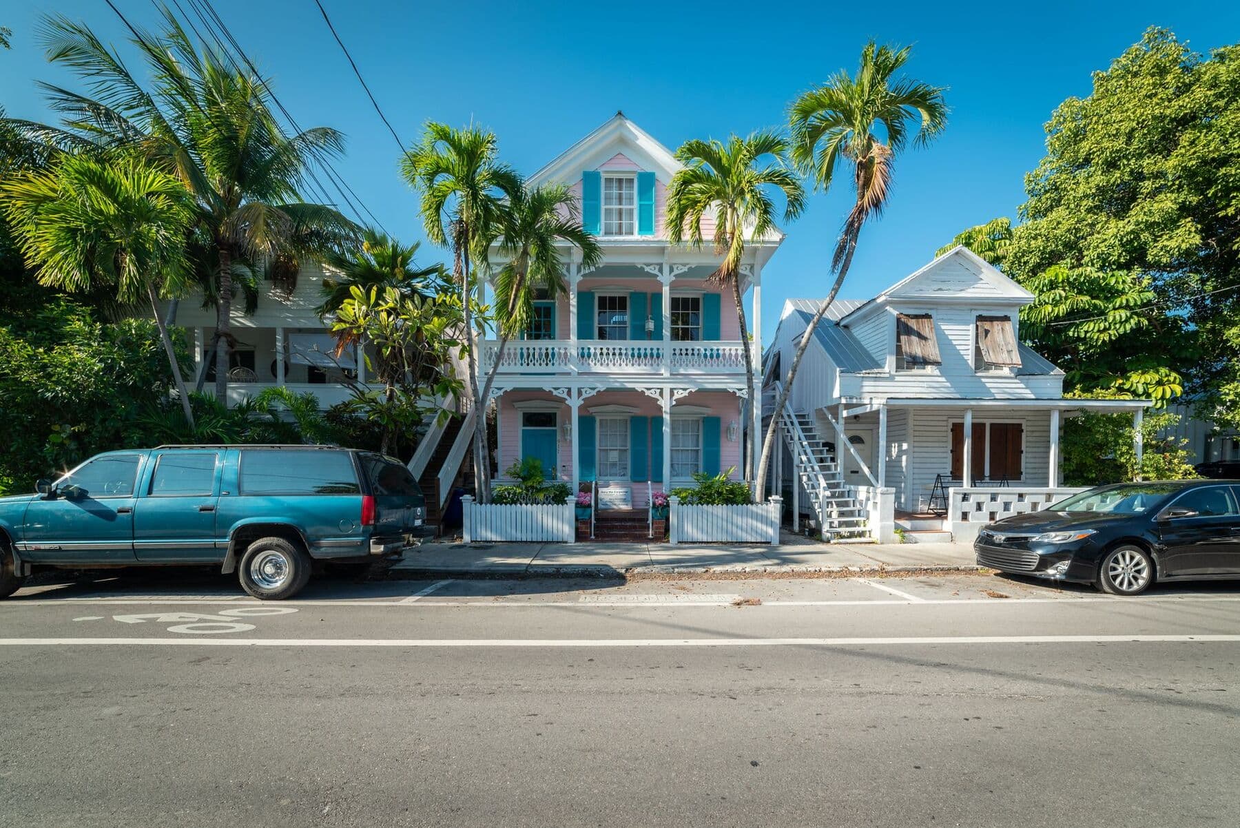 A pastel two-story wooden house with a porch and shutters, among palm trees on a street in Key West, Florida.