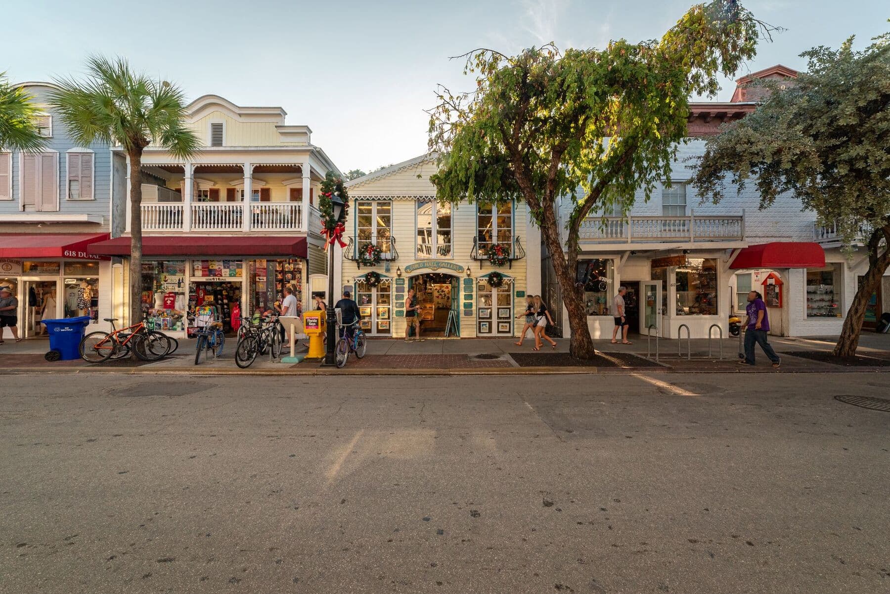 Two-story shopfronts with porches, awnings and parked bicycles on Duval Street in Key West, Florida, at dusk.
