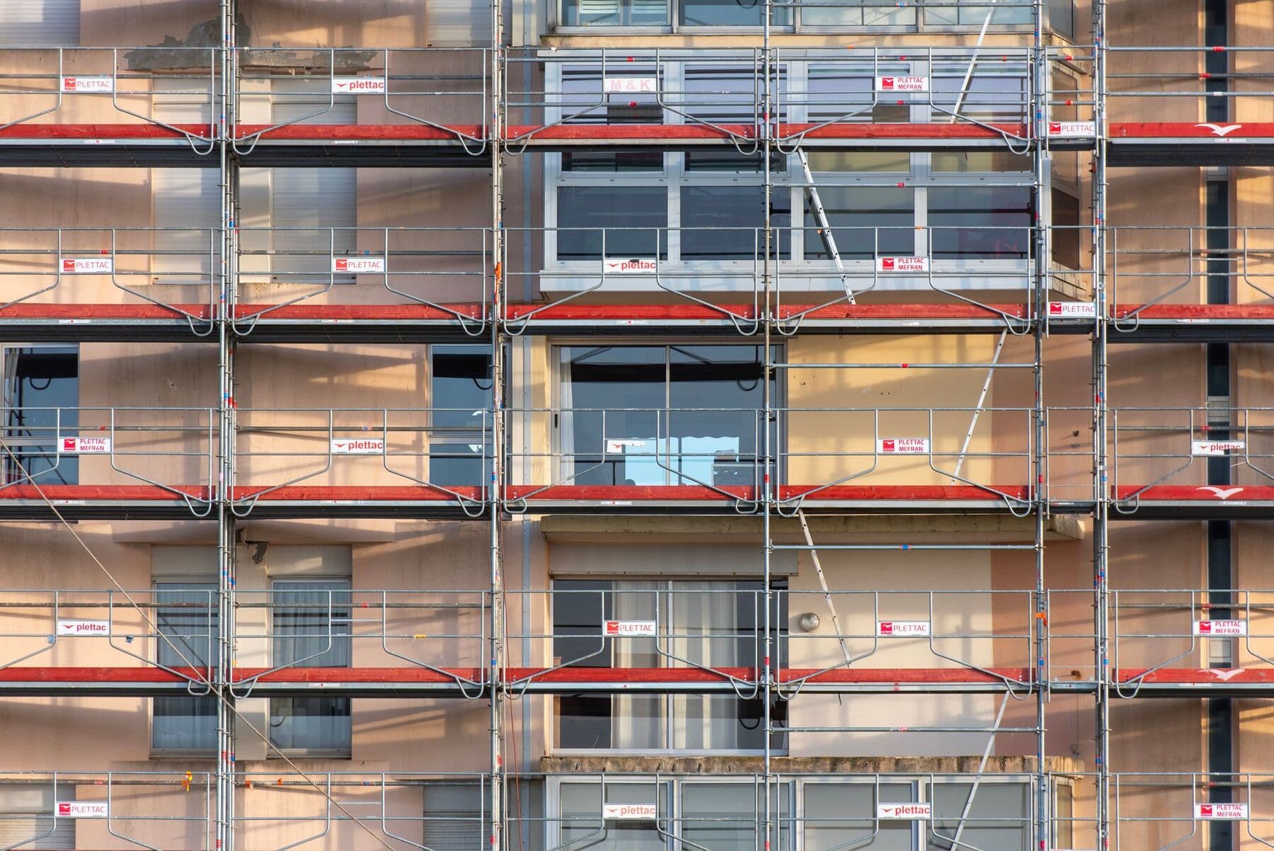 Steel scaffolding with red cross-braces covering the front of a multi-story building.