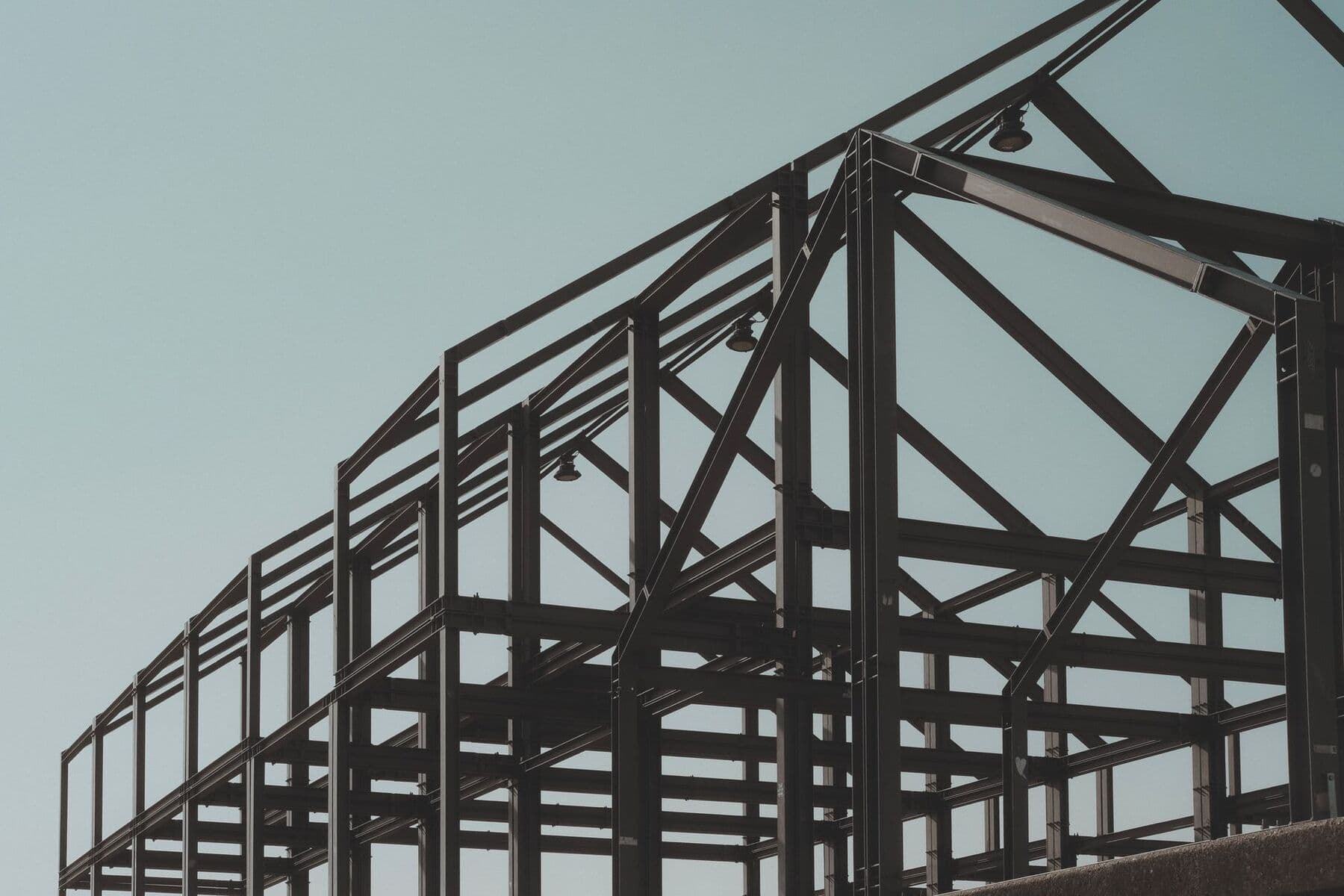 A steel frame of beams and posts rising against a pale gray-blue sky.